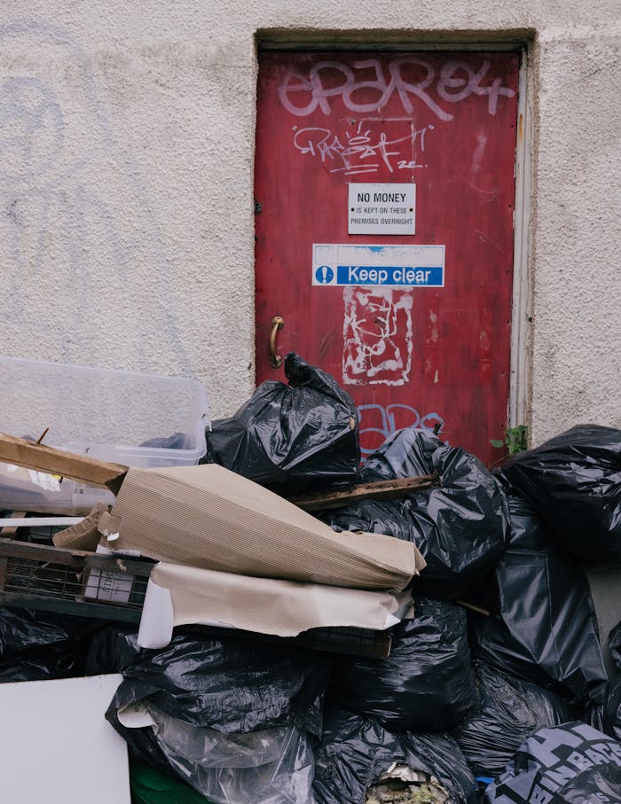 A pile of garbage in front of a graffiti-covered red door with urban decay elements.